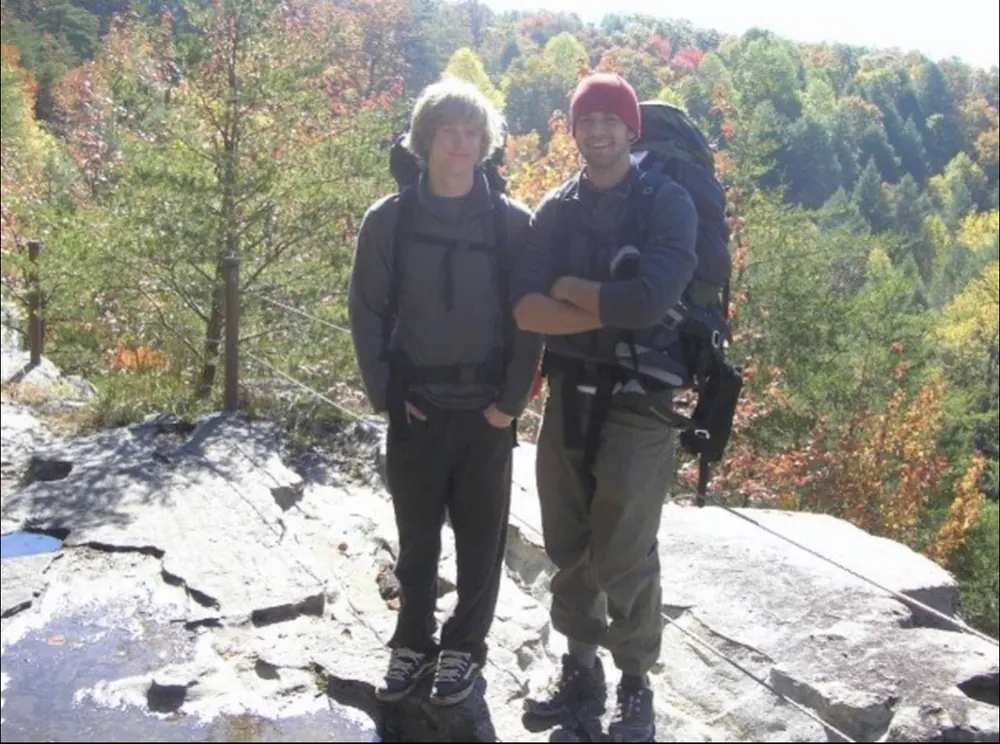 Two backpackers on a rocky overlook with autumn trees