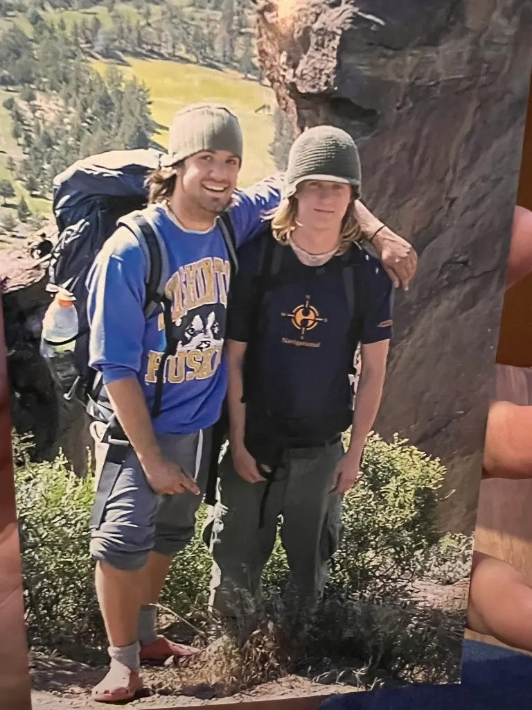 An older printed photograph of two backpackers beside a rock face