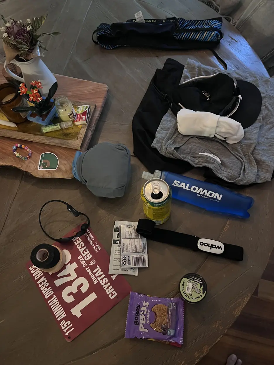 Race gear laid out on a table, including Nathan belt, Salomon flask, Wahoo chest strap, clothes, tape, snack and race bib