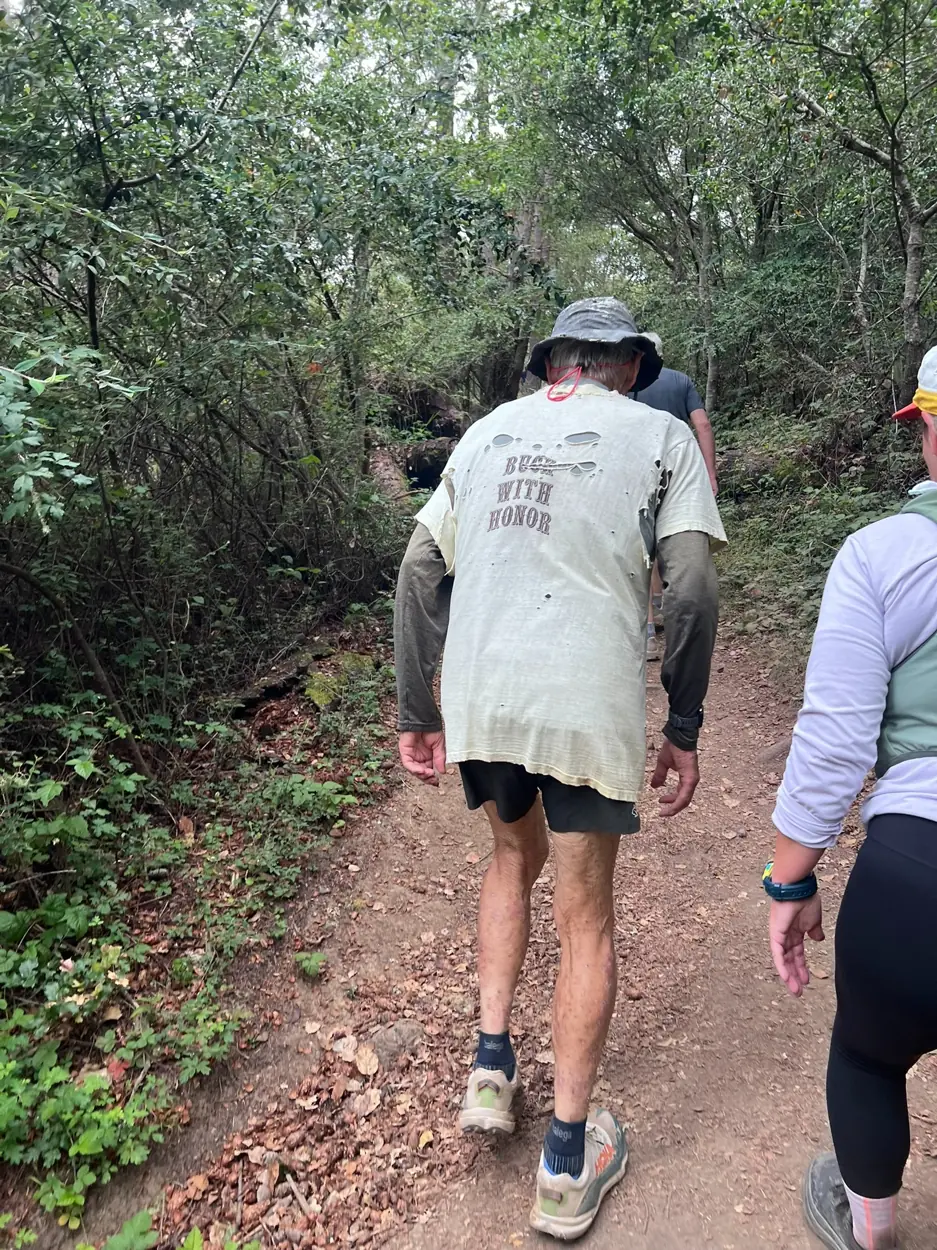 Runners moving along a narrow dirt trail beneath dense green foliage
